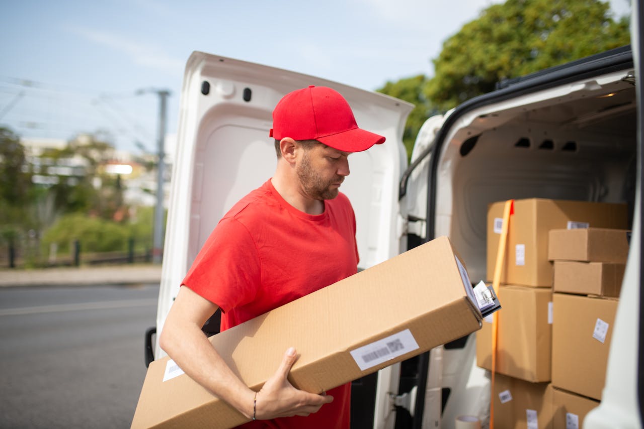 services-02 Courier in red uniform unloading packages from a delivery van on a sunny day.