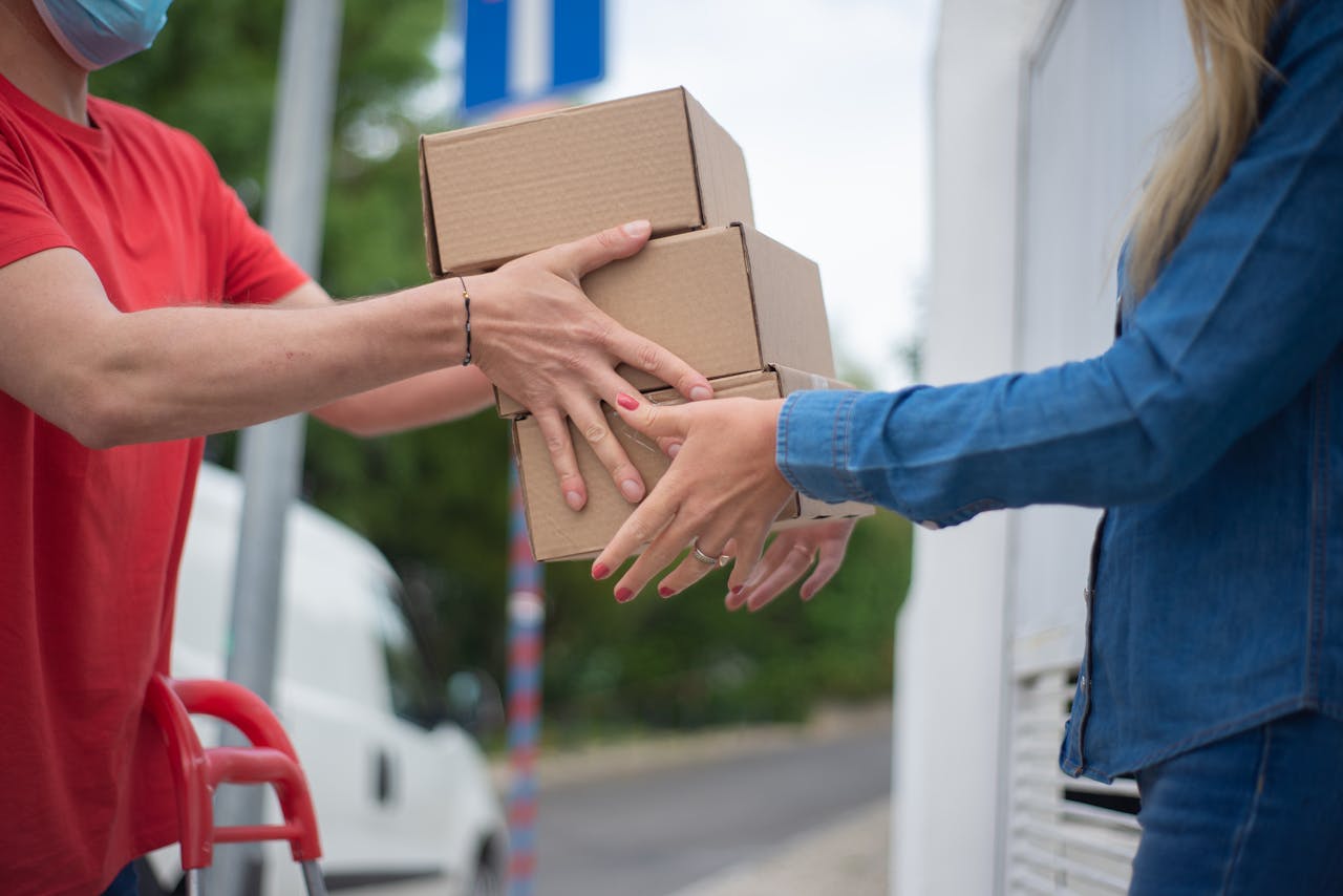 gallery-02 Hands exchanging cardboard boxes during an outdoor delivery scene.